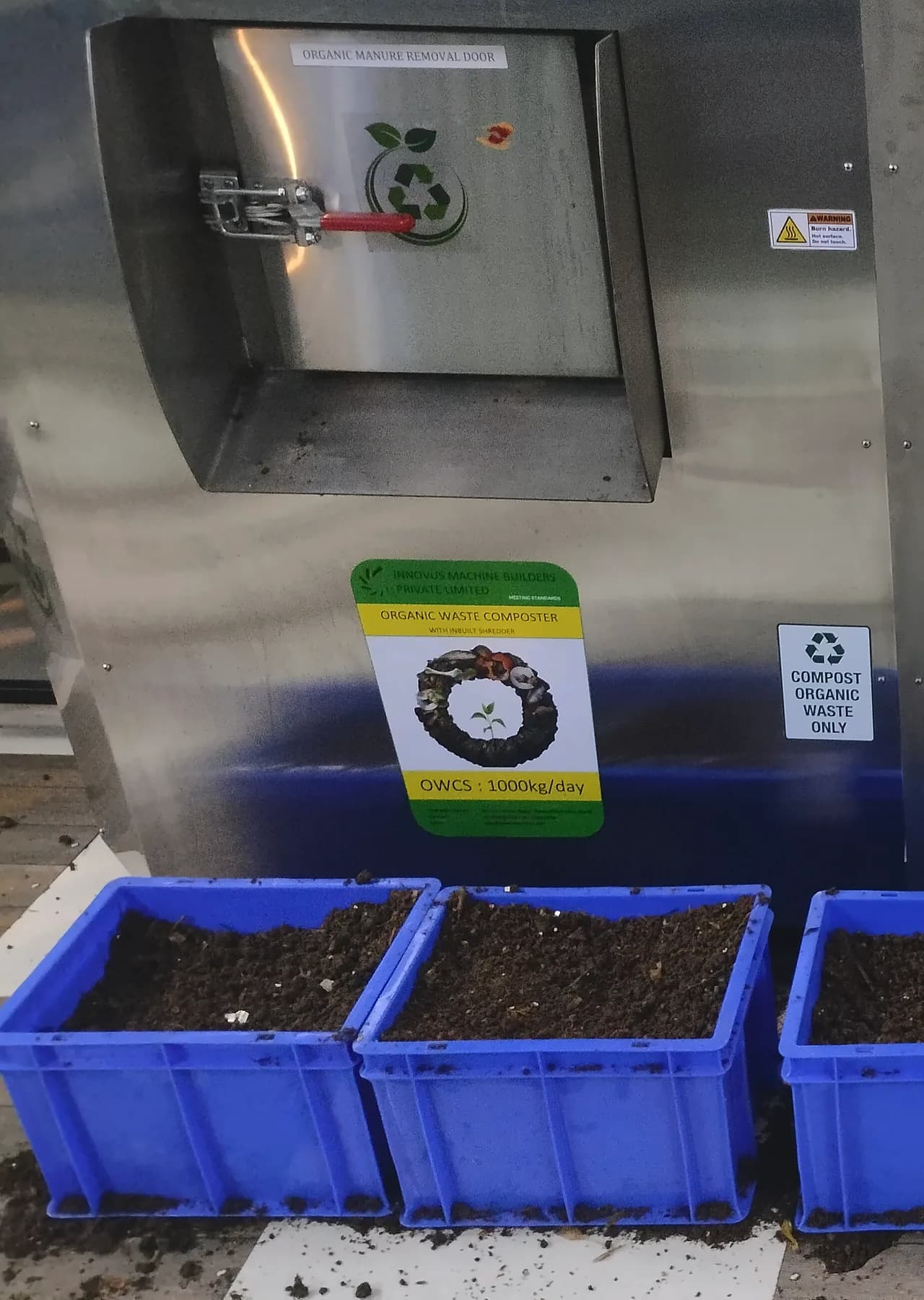 Finished compost in blue crates under an Innovus composter's output door