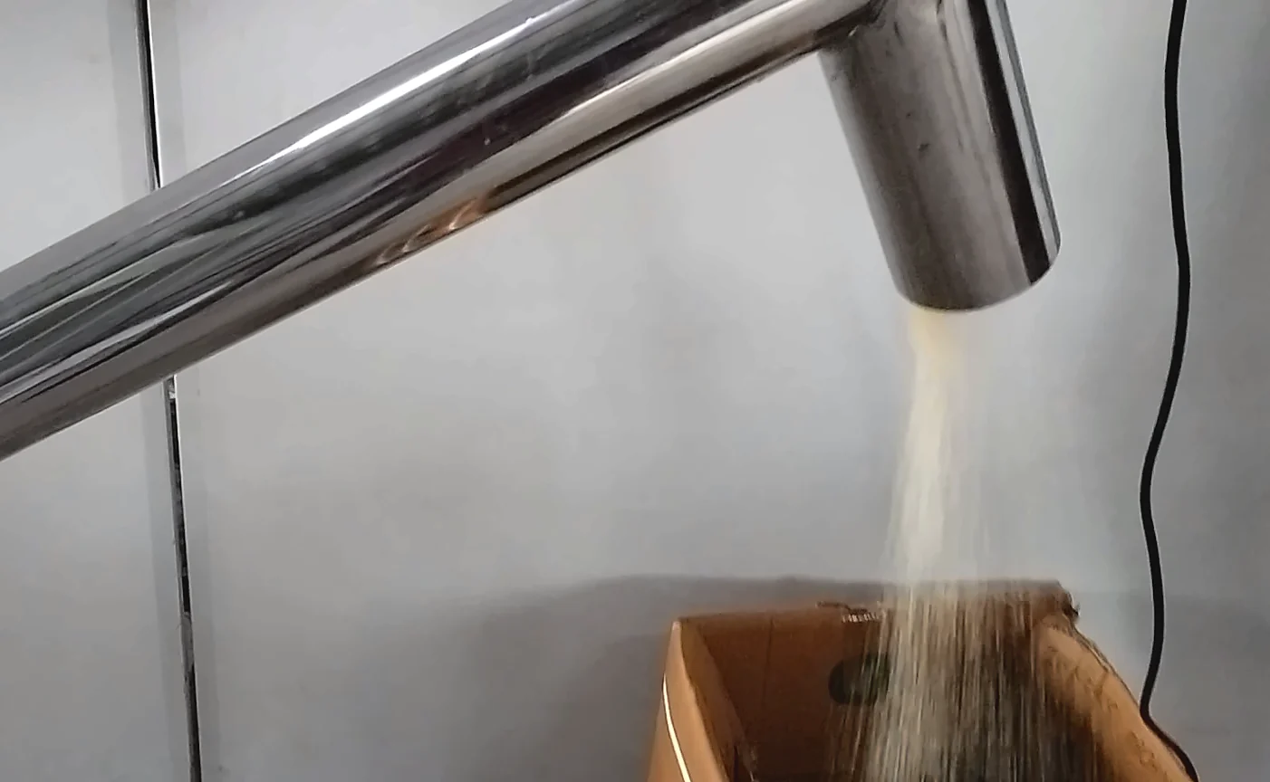 Screw feeder outlet discharging dry material into a box during a test run